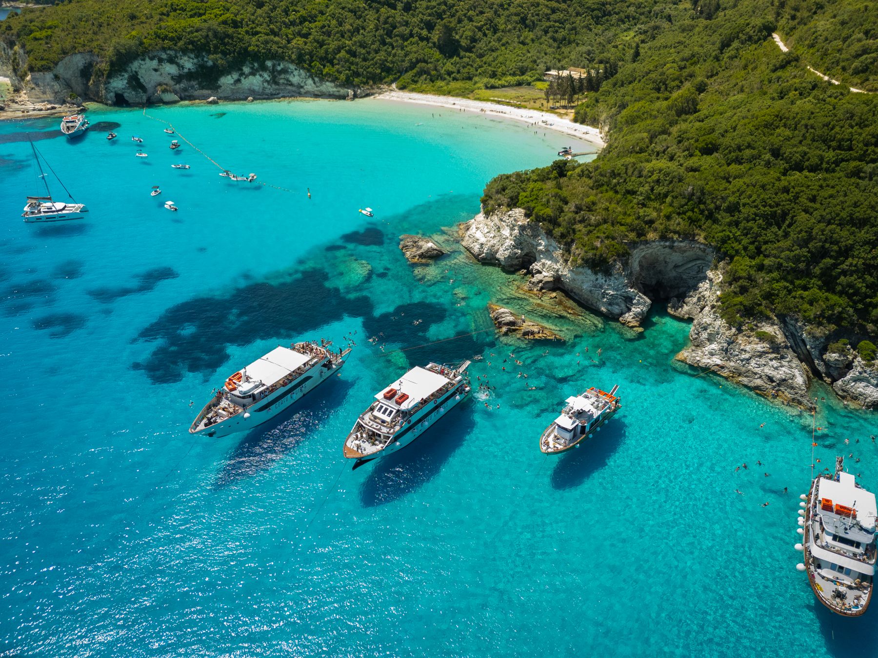 Boats anchored in turquoise water beside a green island coast